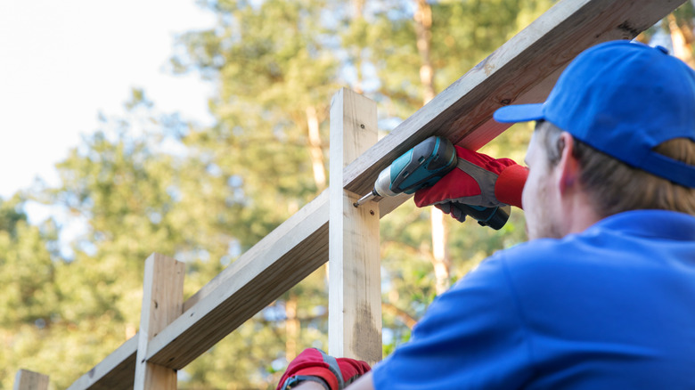 Construction worker in blue shirt building a shed frame from wood