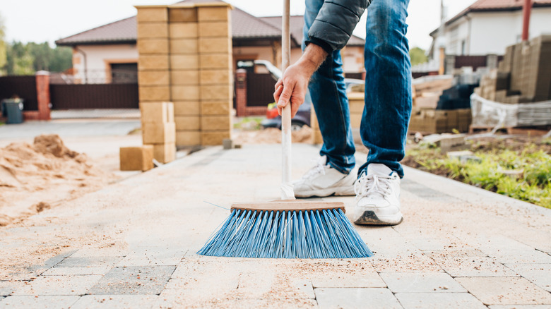 person sweeping pavers with broom