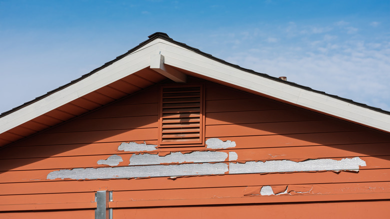 Closeup of a red wooden exterior wall with peeling paint near the roofline.