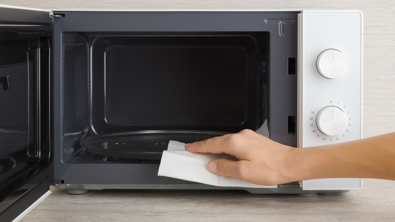 Person wiping out inside of microwave