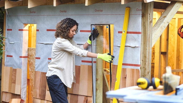 Person fits a window into the opening of a wooden shed in the process of being built