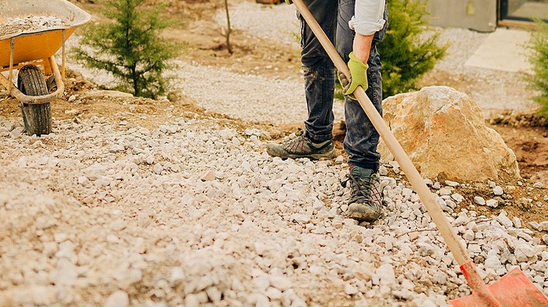 A person prepares foundation for a DIY project with a wheelbarrow of materials seen in the background