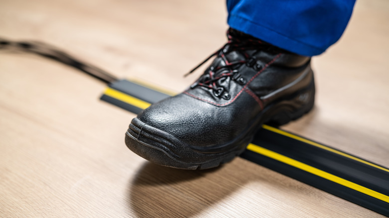 Foot stepping on floor cable protector covering extension cord