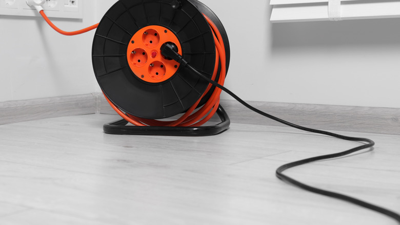 Extension cord reel plugged into power strip on grey floor indoors