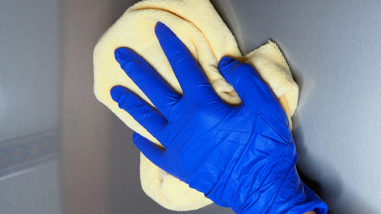 Blue gloved hand drying stainless steel with yellow cloth