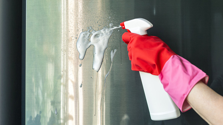 Hand spraying a cleaning agent on stainless steel refrigerator