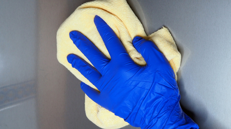 A blue gloved hand wiping stainless steel with microfiber cloth