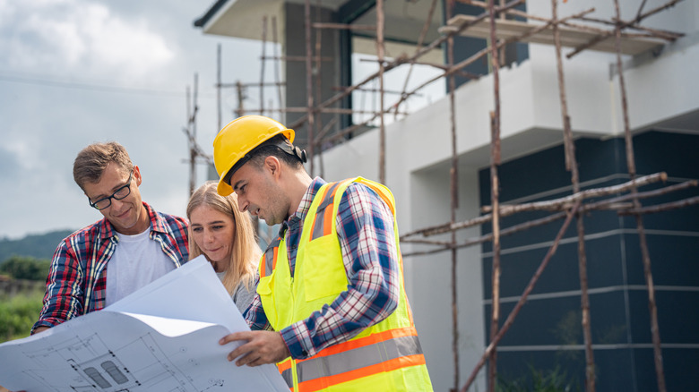 Homeowners and their contractor look over renovation plans outside their home project