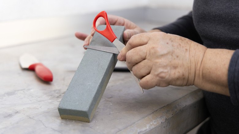 A woman sharpening scissors on a whetstone.