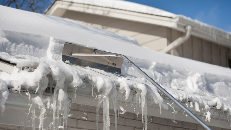 A man removing snow from a roof with a roof rake