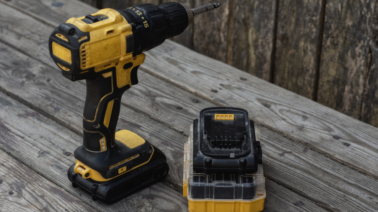 Yellow Cordless electric drill and battery charger on wooden background for DIY projects and repairs
