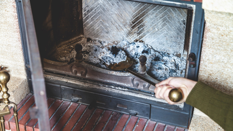 Person scooping the ashes in a fireplace with a shovel