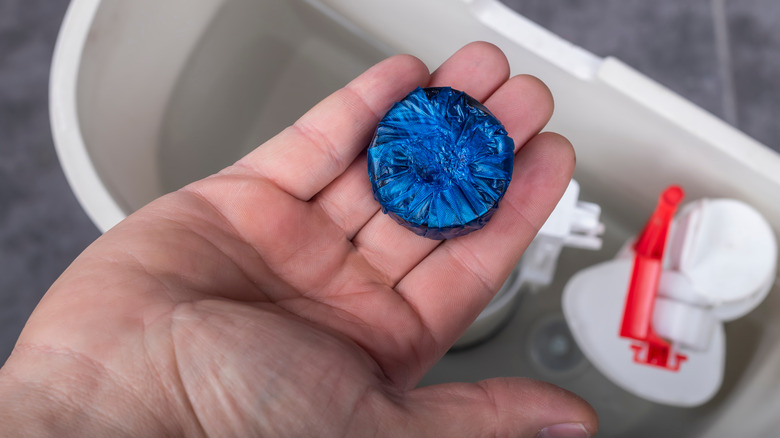Person's hand holding a blue toilet cleaning tablet