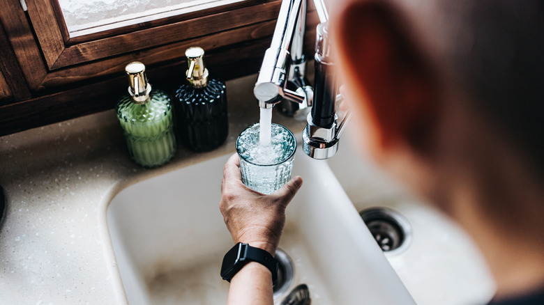 Person filling a glass with water from kitchen sink