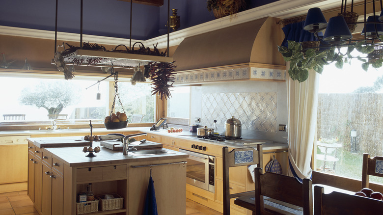 Cozy kitchen with tile backsplash, hanging chandelier lights, wooden island.