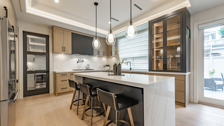 Modern kitchen with brown and black cabinets, white countertops, and three stools