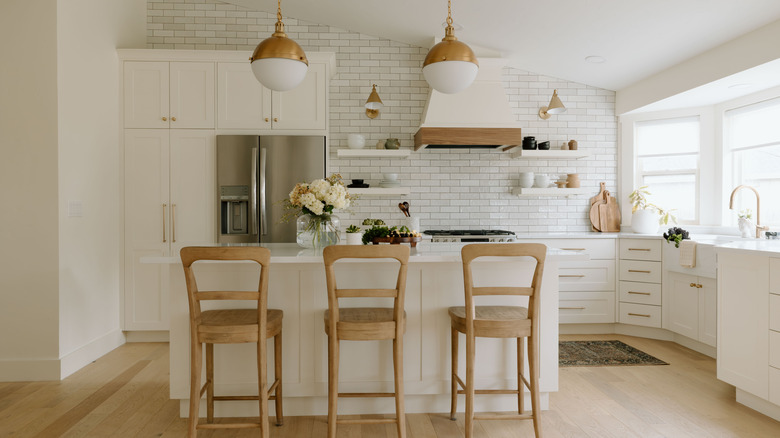 All-white kitchen with wood bar chairs, brass hardware, backsplash, and wood accent tile