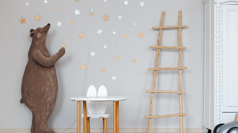 Starry wallpaper in a children's room with a wooden ladder and bear cut-out on either side of a small table and chair