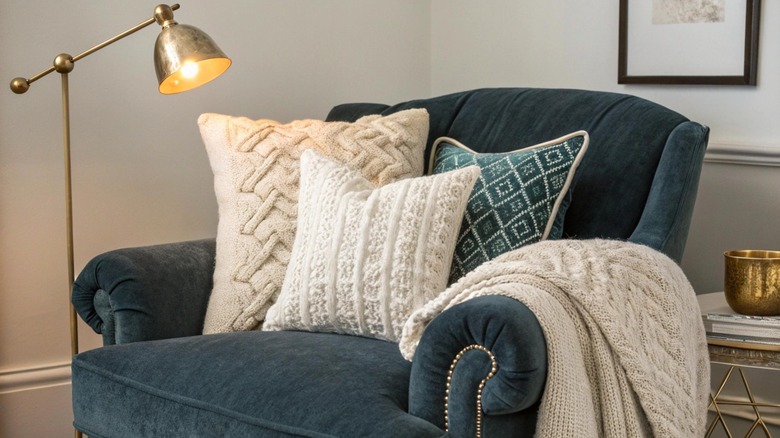 A floor lamp near a cozy recliner with pillows and a throw blanket.