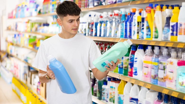 Young man comparing laundry products on store shelf