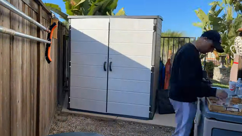 Person standing next to storage shed by wooden fence