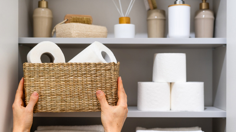A person placing a basket of toilet paper on a bathroom shelf