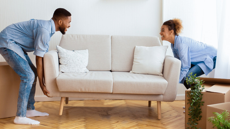 two people moving a light beige couch to a new location