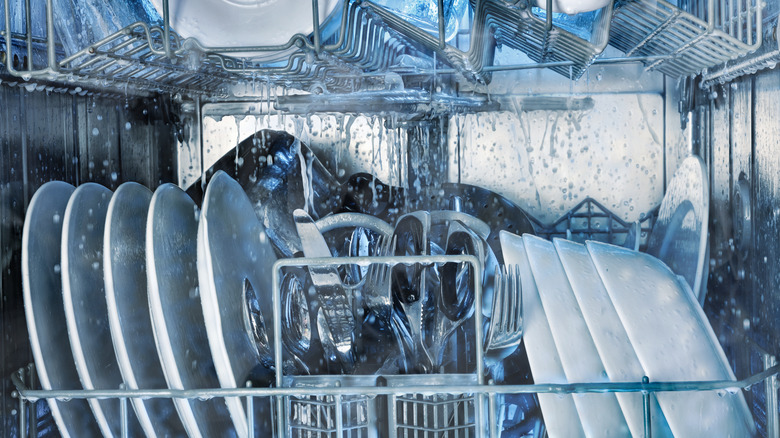 Details of the interior of a running dishwasher washing tableware with grey and blue tones.