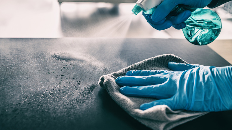 Close-up of a person with gloves disinfecting a black countertop