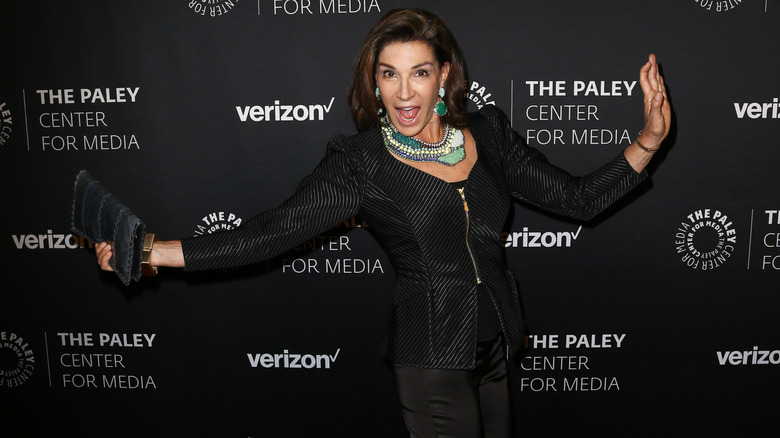 Hilary Farr striking a playful pose with arms outstretched on a red carpet