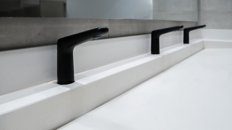 White solid surface bathroom sink with three black faucets