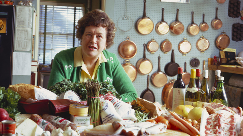 Julia Child sitting in her kitchen surrounded by ingredients.