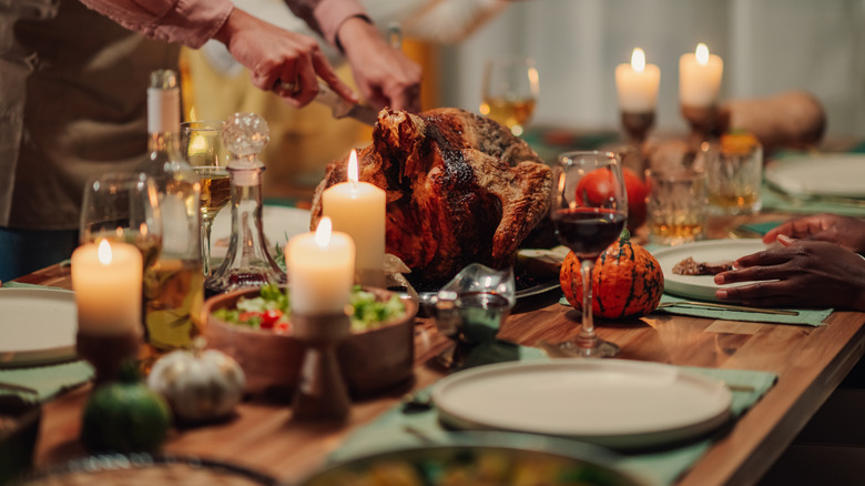 A dinner table at Thanksgiving with someone carving a turkey