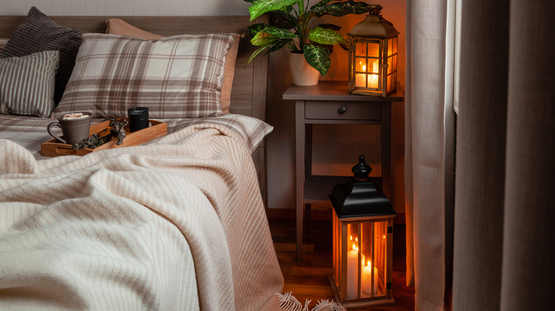 Cozy bedroom with soft candle lights, cozy blankets, and tray with drink on it.