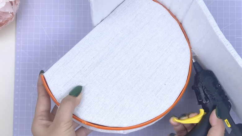 A person glues the the upholstered side of a DIY box to the base.