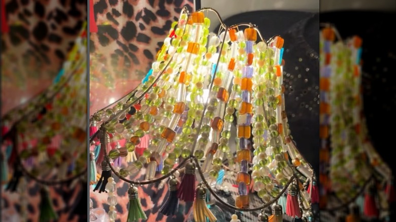 An old lampshade is upgraded with strings of beads in various shapes and colors.