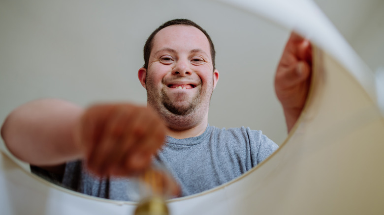 A smiling man removes a lampshade from a lamp.
