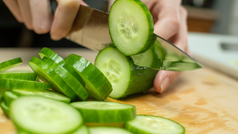Women's hands cut a fresh cucumber into circles on a wooden Board close up
