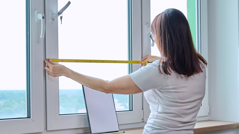 Woman measuring windows before adding curtains