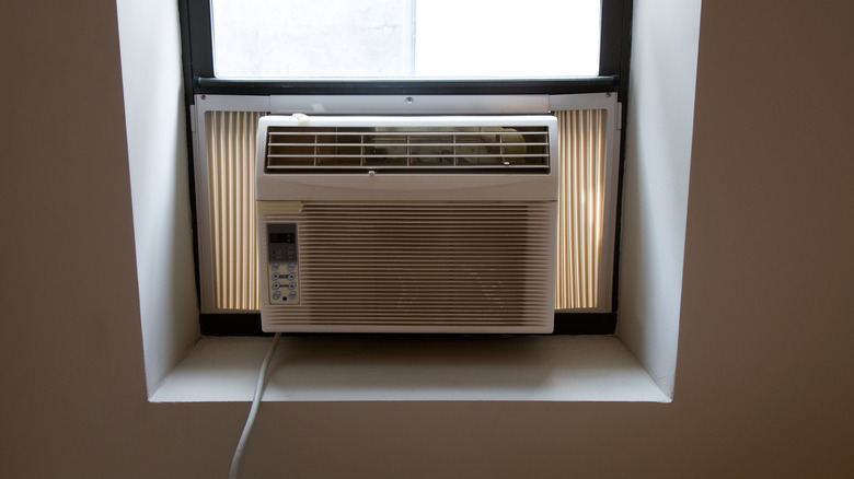 An old-style air conditioner window unit with no curtains around it.