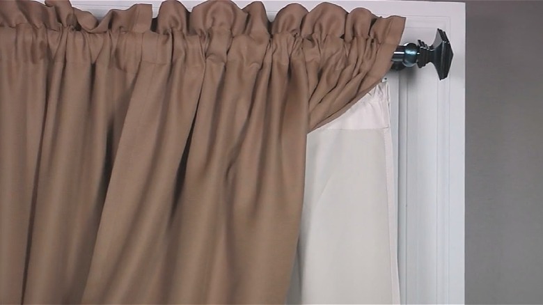 A hanging curtain pulled back to reveal a white curtain liner insulating the window.
