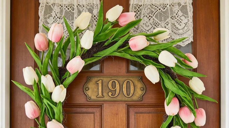 A faux tulip wreath with pink blooms hanging on a wooden front door