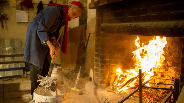 man cleaning ash from burning fireplace