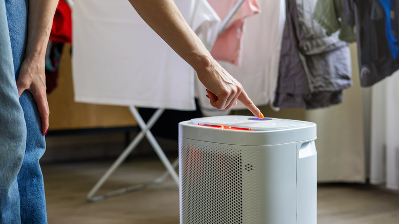 Close up of a person turning on a portable dehumidifier with laundry hanging in the background