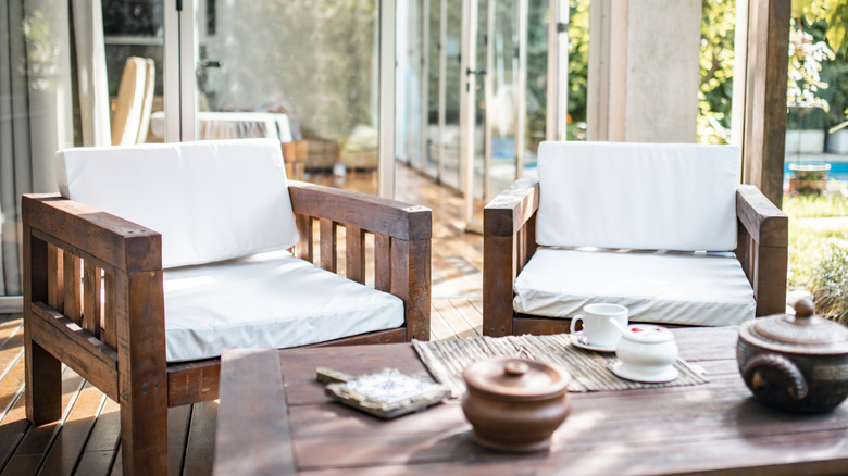 A couple of teak outdoor chairs with white cushions