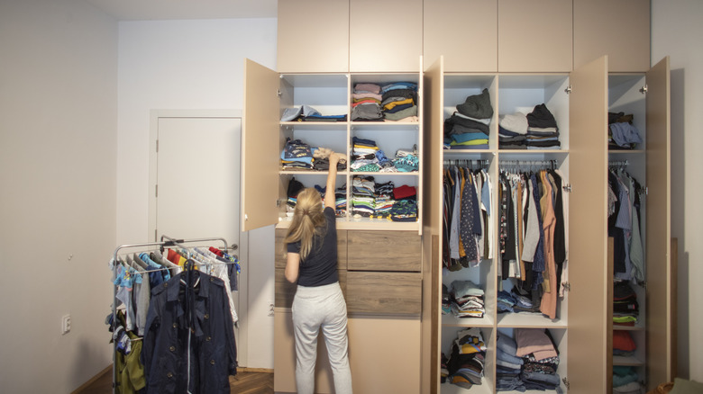 Woman reaching for a clothes on a shelf in a closed closet wardrobe system