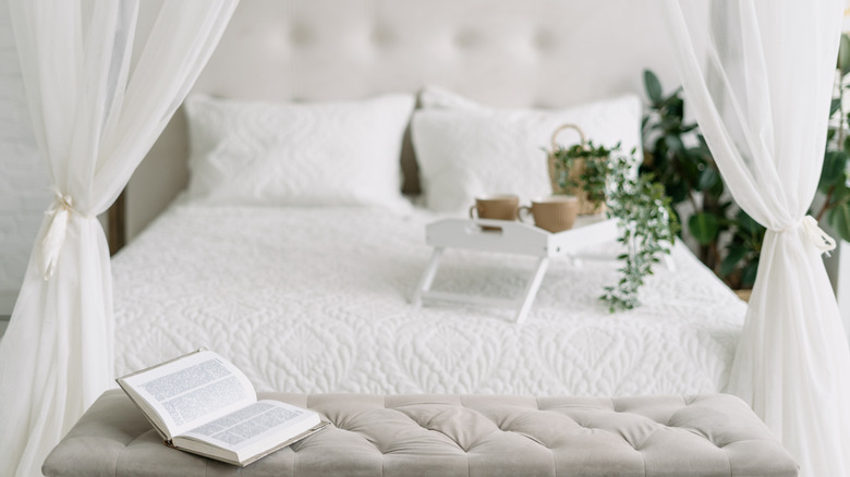 White canopy bed in bedroom with tufted bench and drink tray