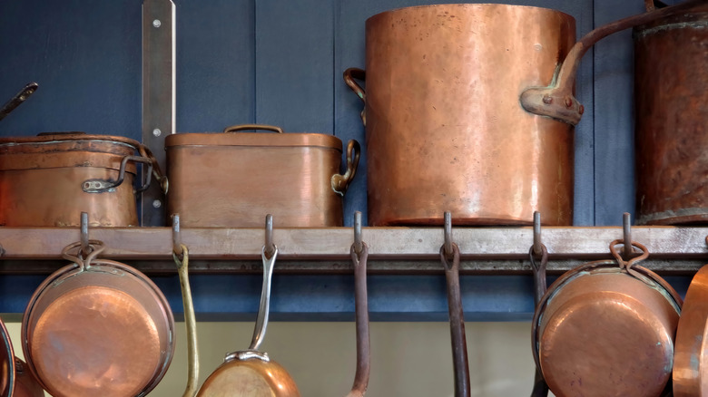 A shelf of tarnished copper pots and pans that need cleaning.