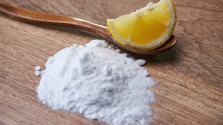 A slice of lemon and tablespoon of cream of tartar on a wood table.
