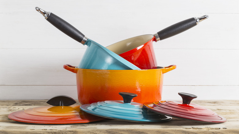 A stack of colorful pots, pans, and lids sit on a counter in a kitchen.